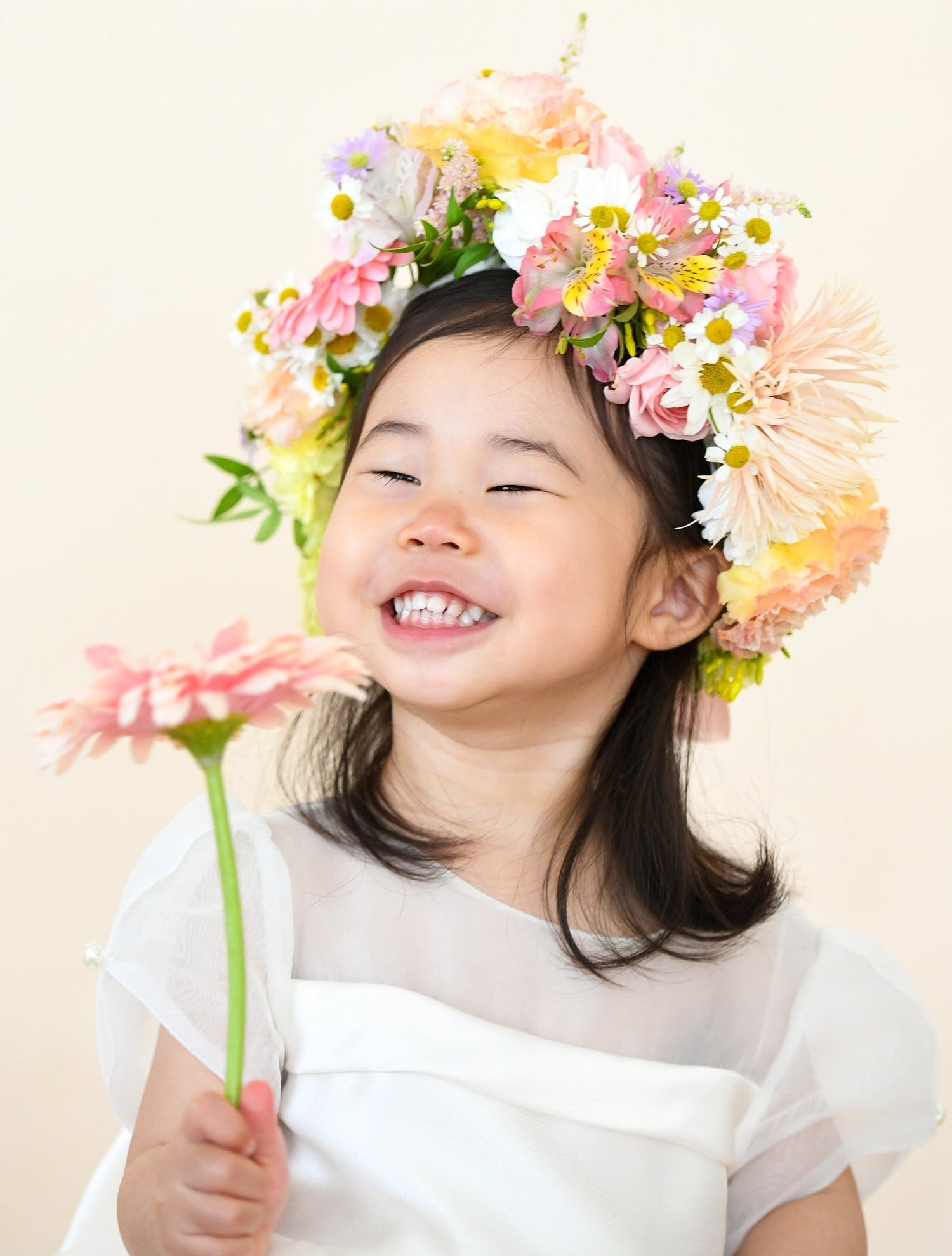 Young girl with a floral headband and flower in her hand against a light background